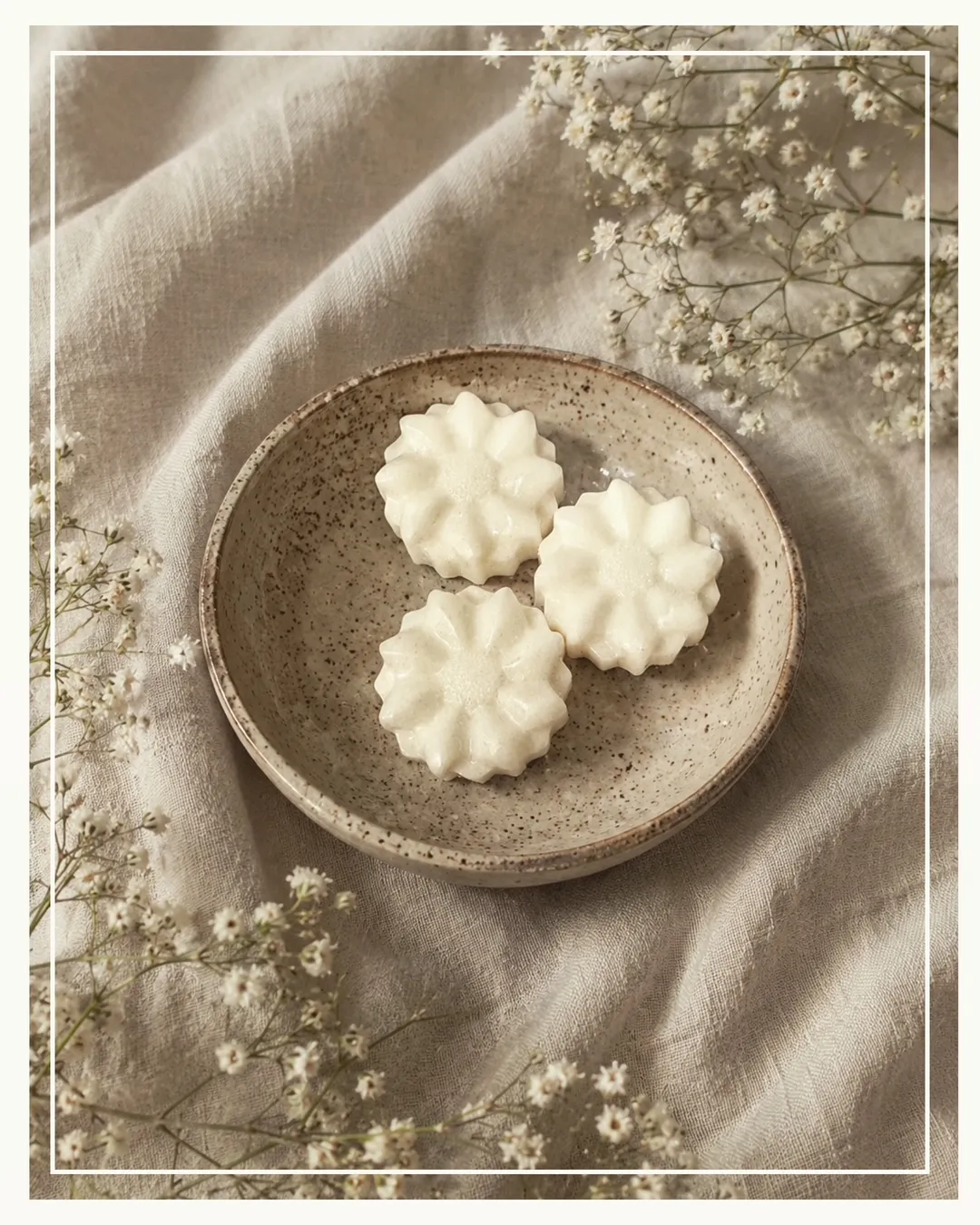 Cream flower-shaped wax melts resting in a speckled ceramic dish